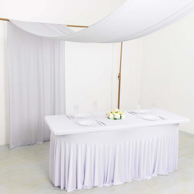 Elegant white table setup with draped fabric and floral centerpiece.