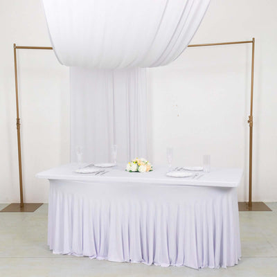 Elegant white table setup with draped fabric and floral centerpiece.