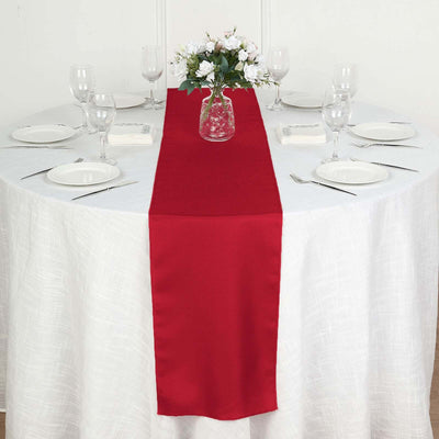 Red table runner on a round dining table set for a meal with floral centerpiece.
