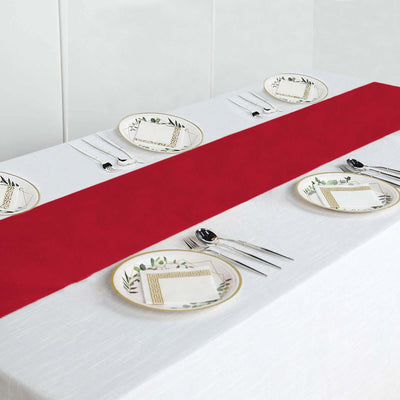 Red table runner on a dining table set with decorative plates and cutlery.