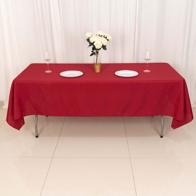 Red tablecloth with plates and glasses set on a dining table.
