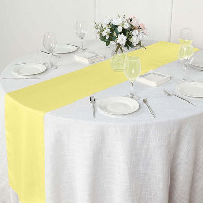 Yellow table runner on a round table set for dining with glassware and flowers.