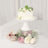 Acrylic cake stand with a white cake and fresh flowers beneath it.