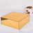 Gold rectangular box on a white table with a cake in the background.
