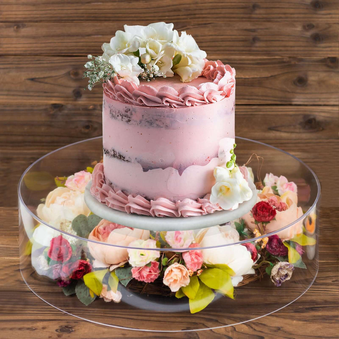 Pink floral cake on a decorative stand with flowers.
