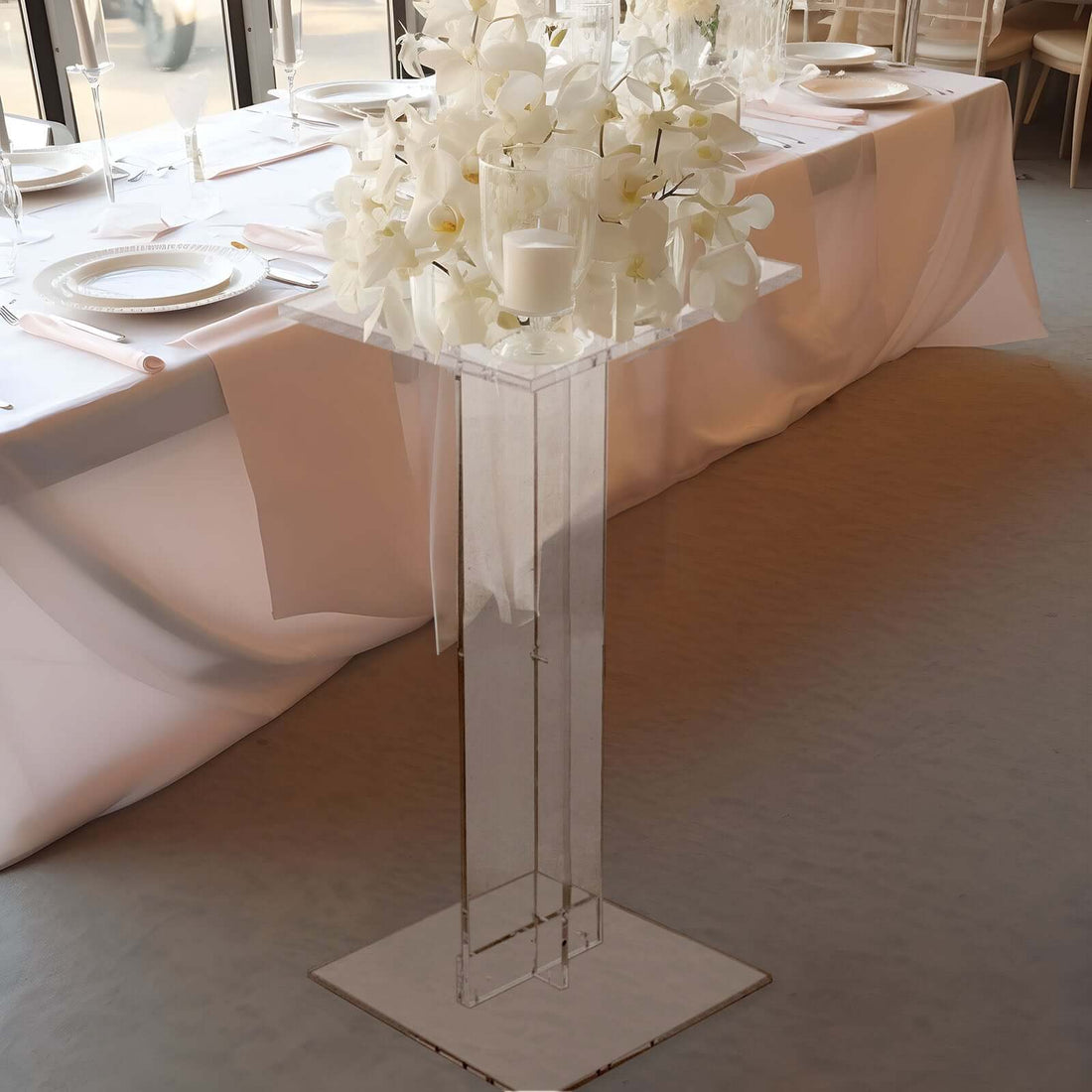 Elegant acrylic pedestal table with white floral arrangement and candles.