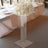 Elegant acrylic pedestal table with white floral arrangement and candles.