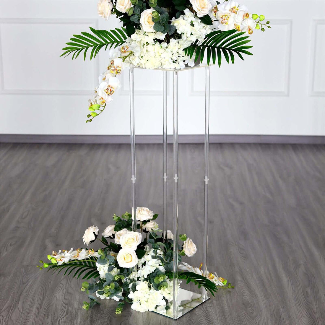 Clear acrylic flower stand with white roses and greenery arrangements.