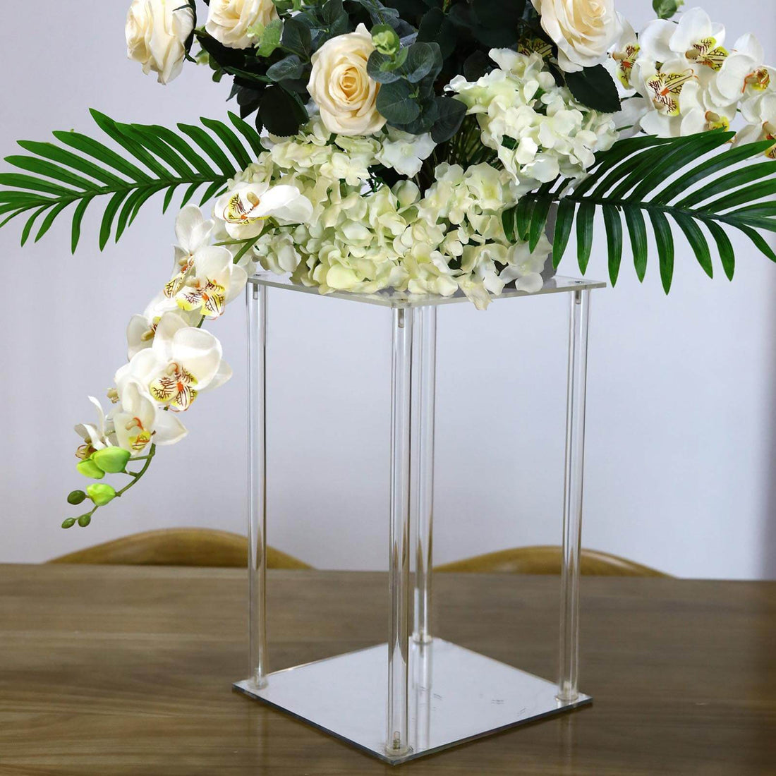 Clear acrylic vase with white roses and orchids, styled with greenery.