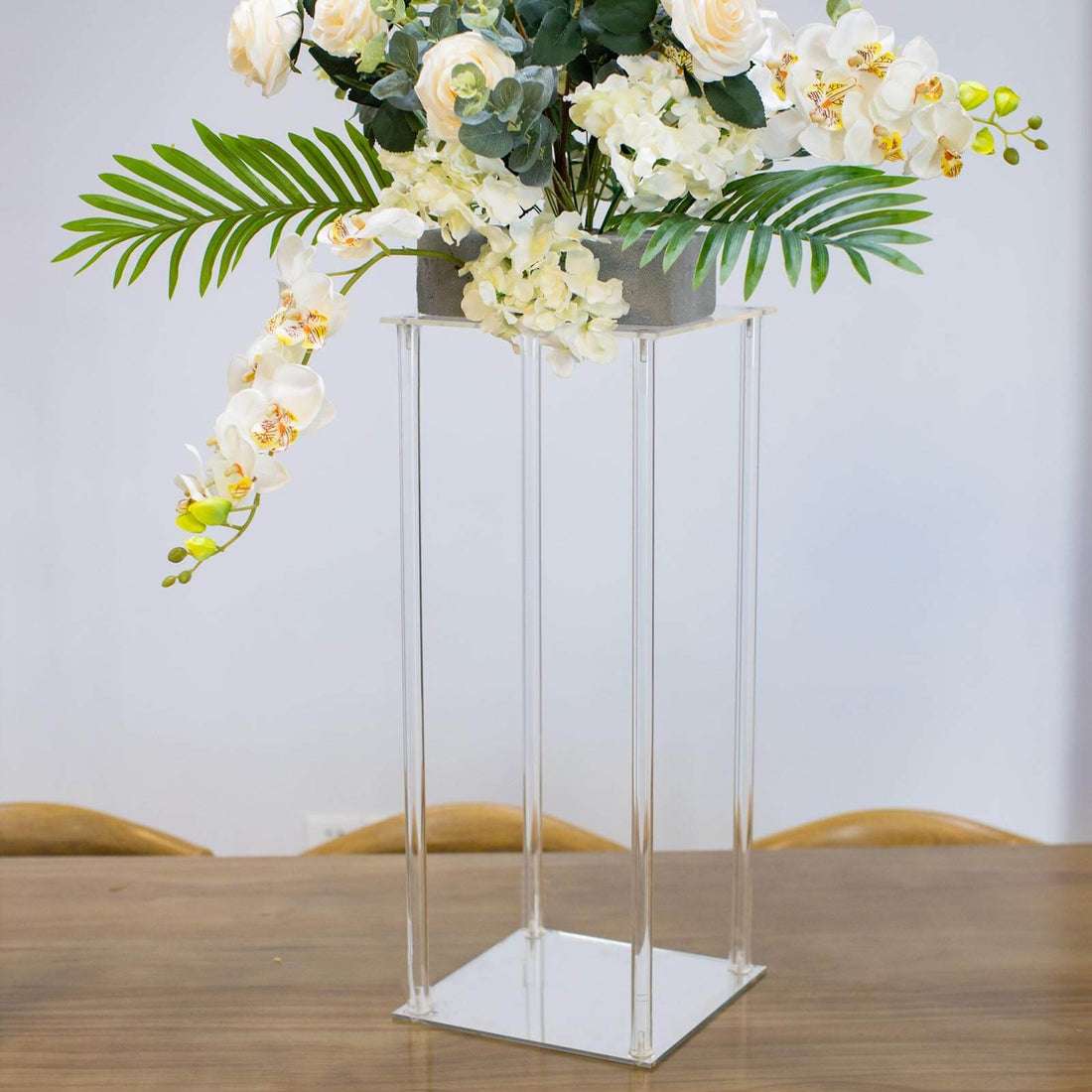 Clear acrylic flower stand with white floral arrangement.