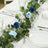 Table setting with blue roses and greenery on a white tablecloth.