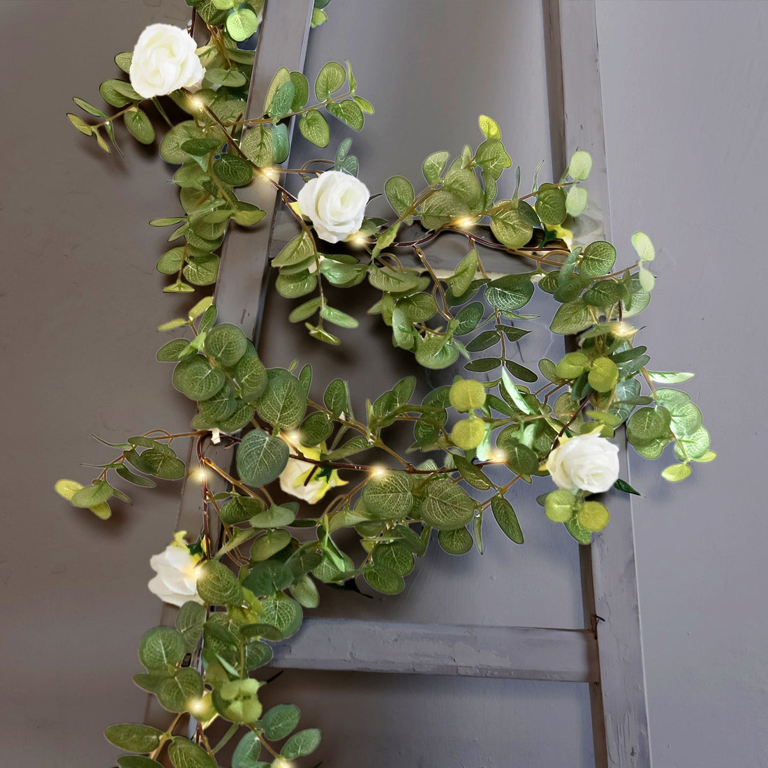 Artificial flower garland with LED lights on a wooden ladder.