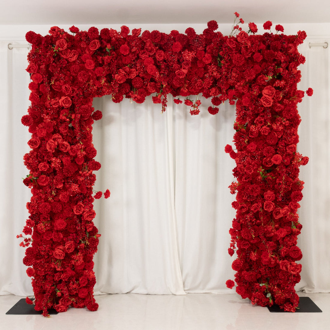 Red floral archway adorned with vibrant roses and blooms against a white backdrop.