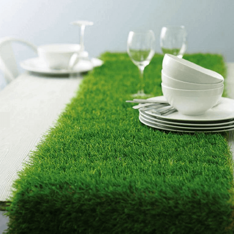 Green grass table runner with white dishware and glasses arranged on a dining table.