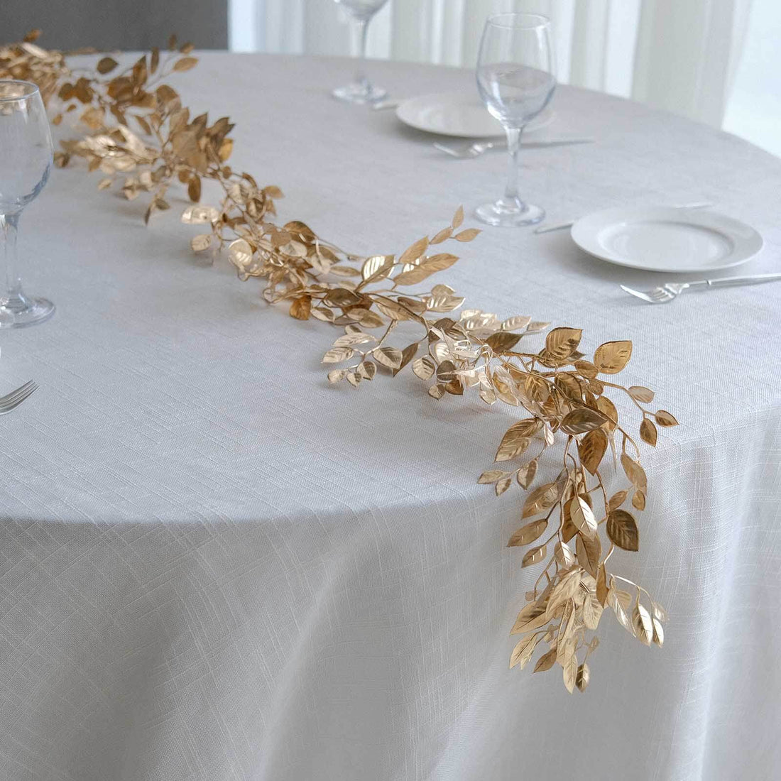 Gold leaf table runner on a white table setting with glassware and plates.
