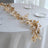 Gold leaf table runner on a white table setting with glassware and plates.