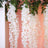 White floral hanging decor with greenery on a soft pink backdrop.