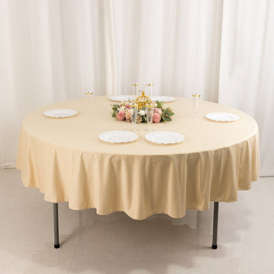 Round table set with beige tablecloth, plates, and floral centerpiece.