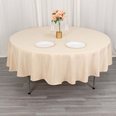 Round beige tablecloth draped over a table set for dining.