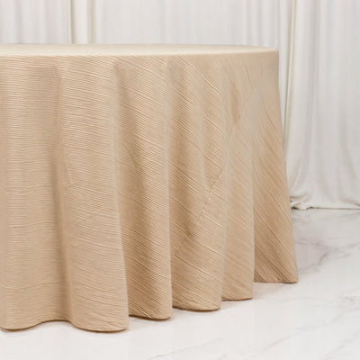 Beige textured round tablecloth draped over a table in a soft white studio