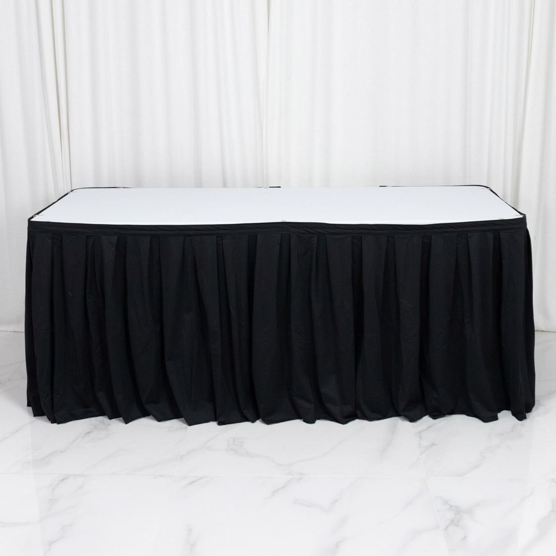Black banquet table with white top and black pleated table skirt on white backdrop