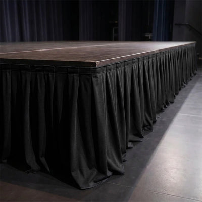 Black draped stage platform with wooden top in dimly lit venue
