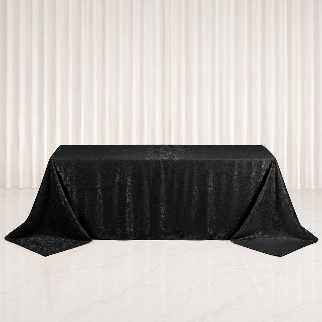 Black jacquard rectangular tablecloth draped over banquet table on white backdrop