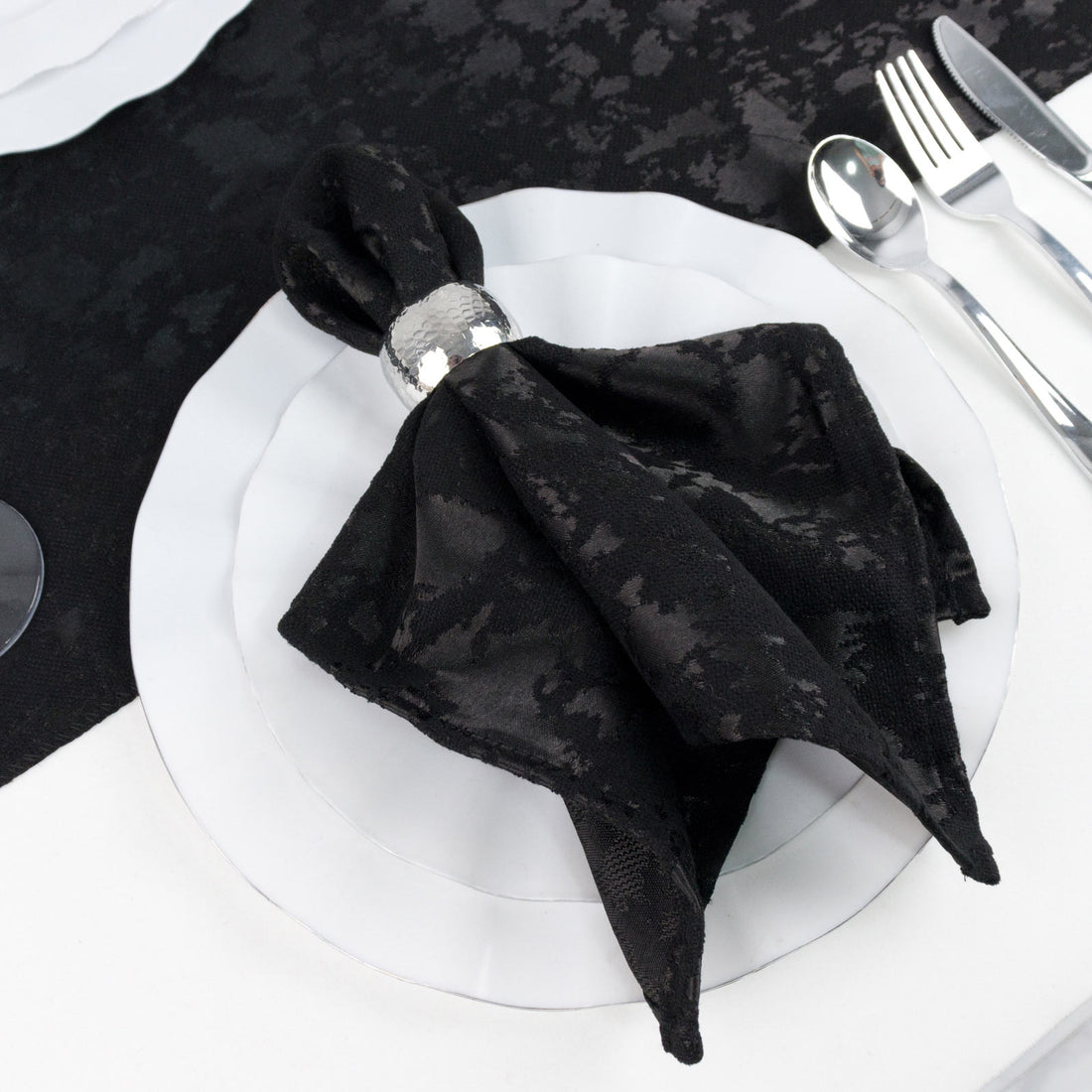 Black napkin folded on white dinner plate with silver cutlery, elegant table setting