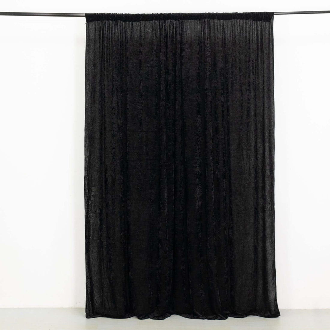 Black velvet curtain draped on a rod against a plain background