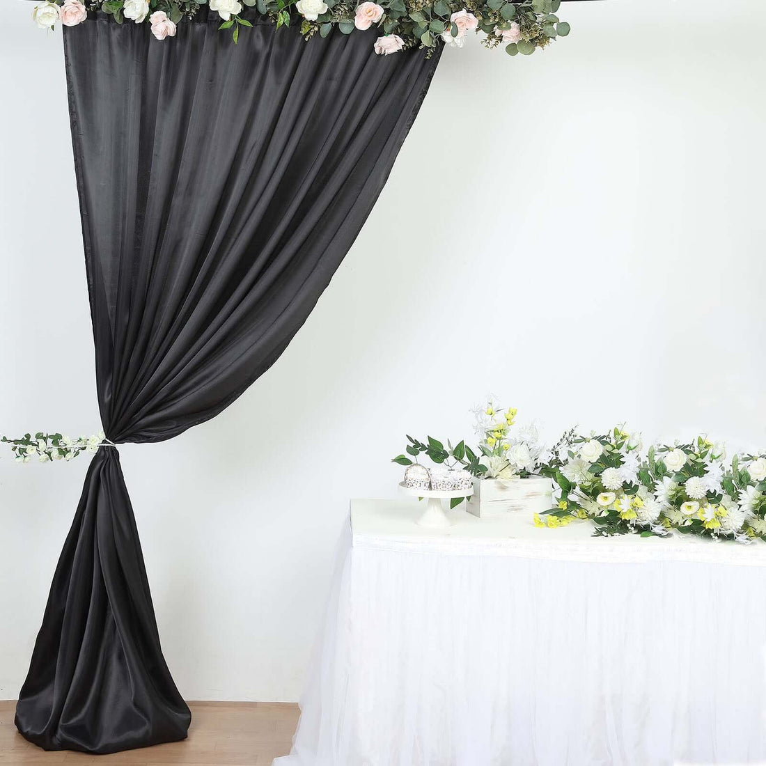 Black drapery with floral decor beside a decorated table of flowers.