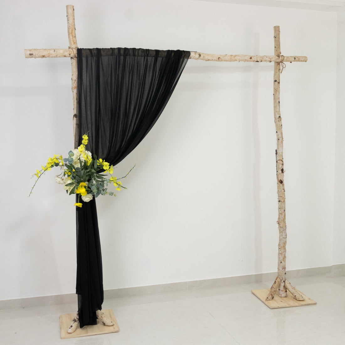 Black drapery backdrop with floral arrangement on a rustic wooden frame.