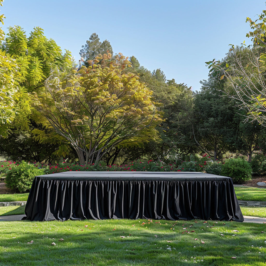 Outdoor event stage with black draped table in a lush garden setting.