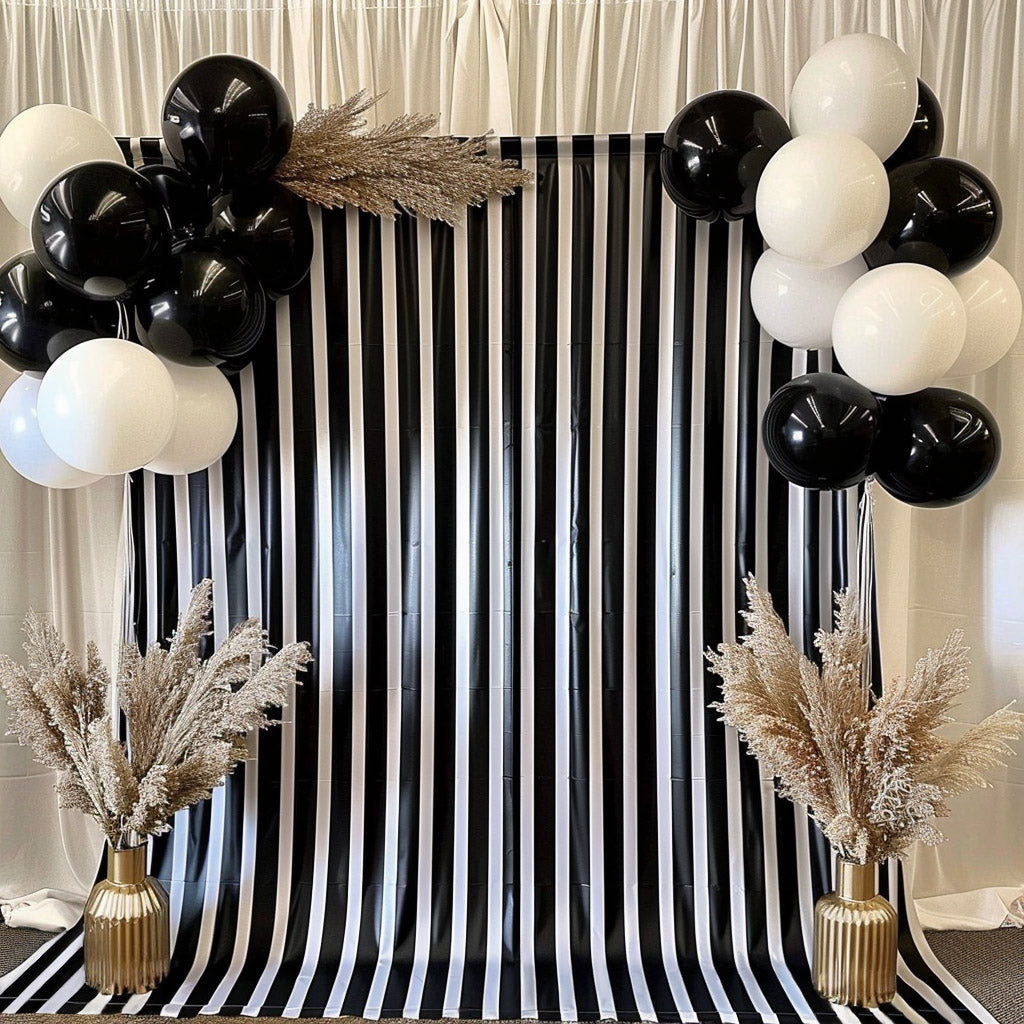 Black and white striped backdrop with balloons and decorative plants.