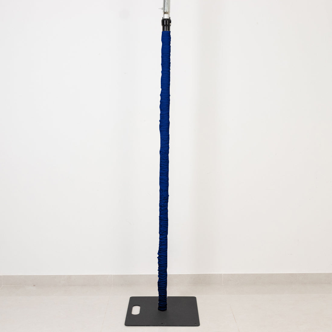 Blue padded vertical pole on a black base against a white wall