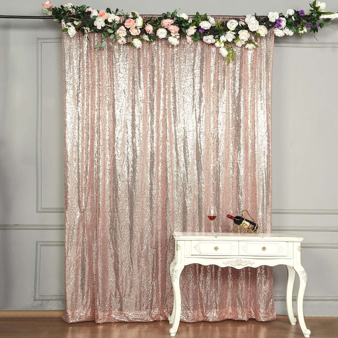 Sparkling rose gold sequin backdrop with floral accents and a white table.