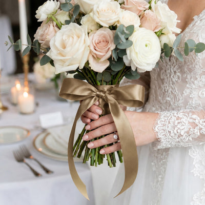 Bride holding elegant blush and white rose wedding bouquet with gold ribbon