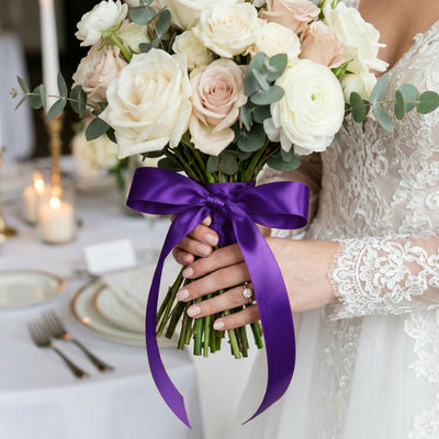 Bride holding ivory rose bouquet with purple ribbon at wedding reception