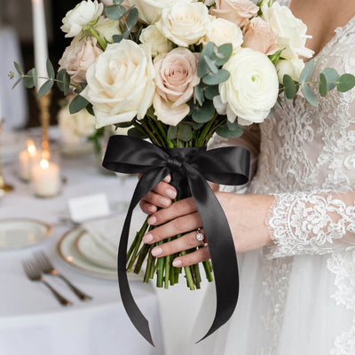 Bride holding ivory rose wedding bouquet with black ribbon bow