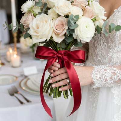 Bride holding ivory rose wedding bouquet with burgundy ribbon