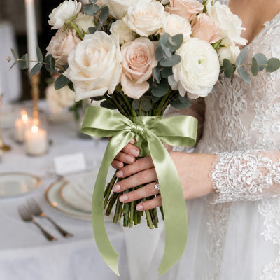 Bride holding pastel rose wedding bouquet with green satin ribbon