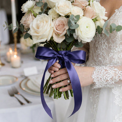 Bride holding white and blush rose bouquet with purple ribbon at wedding