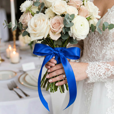 Bride holding white and blush wedding bouquet with blue ribbon