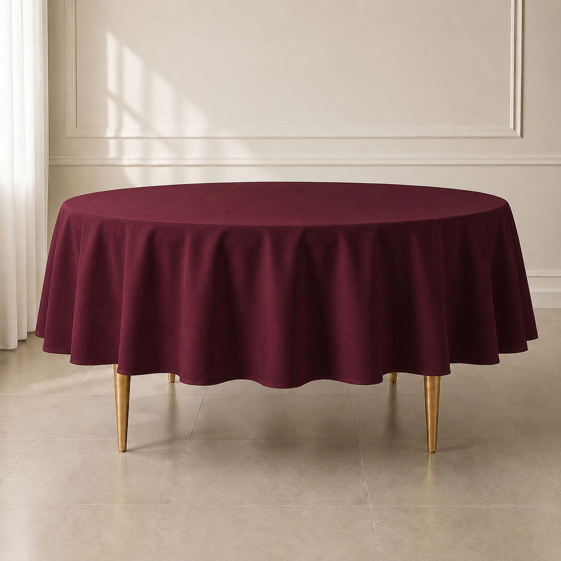 Burgundy round tablecloth on a table in a bright, elegant setting.