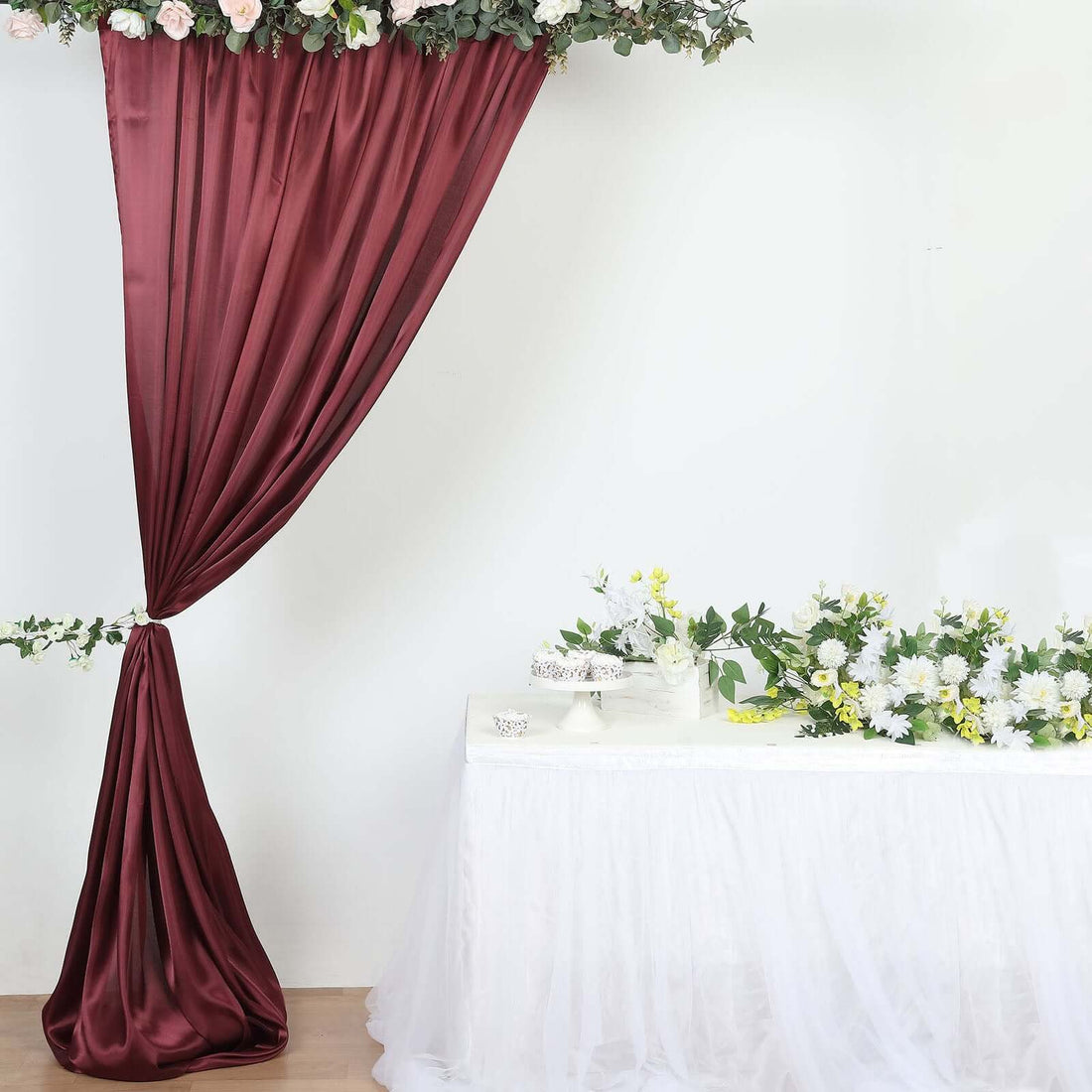 Maroon satin curtain draped elegantly with floral arrangements on a table.