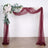 Burgundy wedding arch with floral arrangement and draped fabric