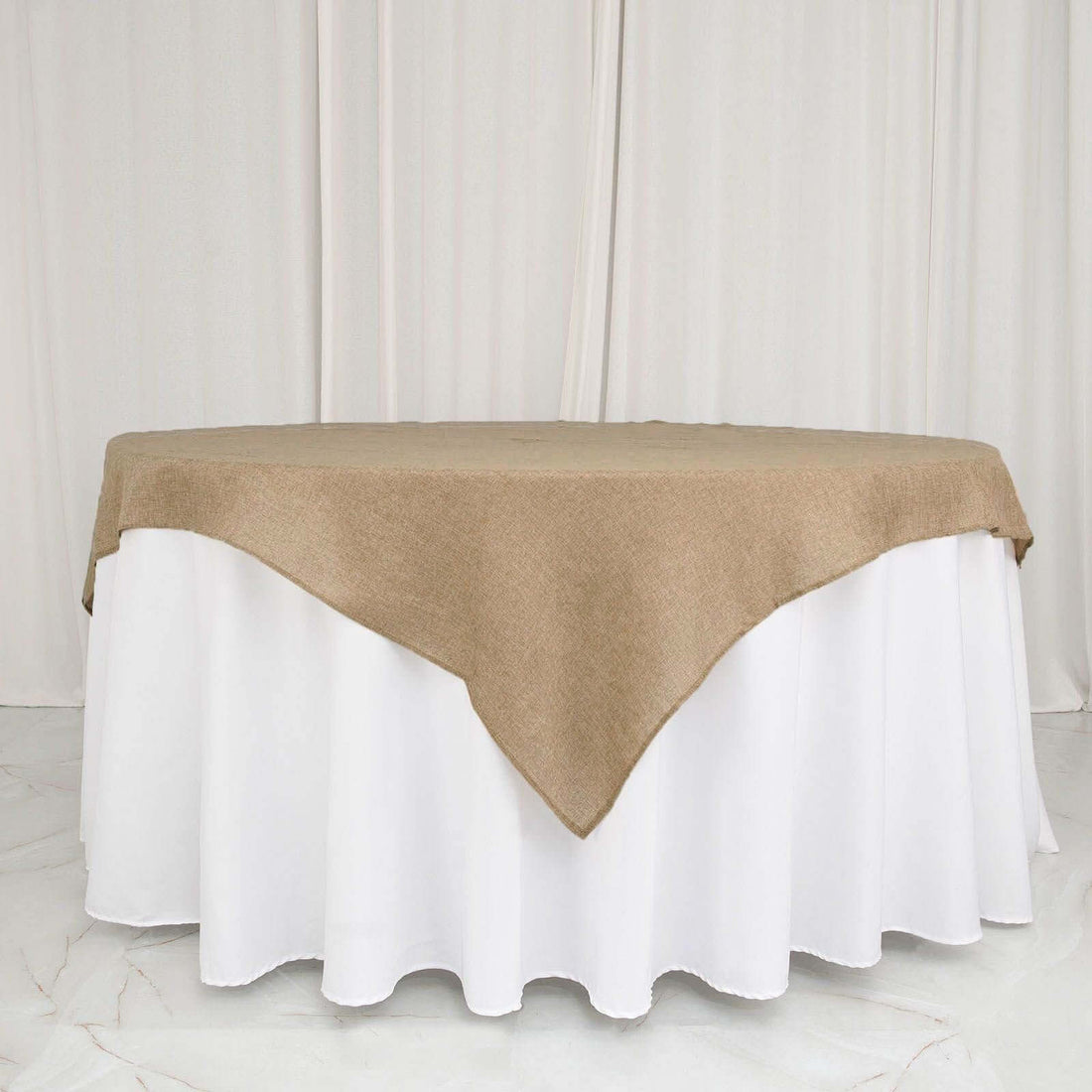 Round table with a beige burlap tablecloth over a white table skirt.