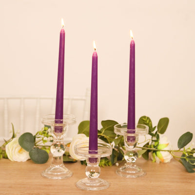 Purple taper candles in glass holders with greenery and flowers.