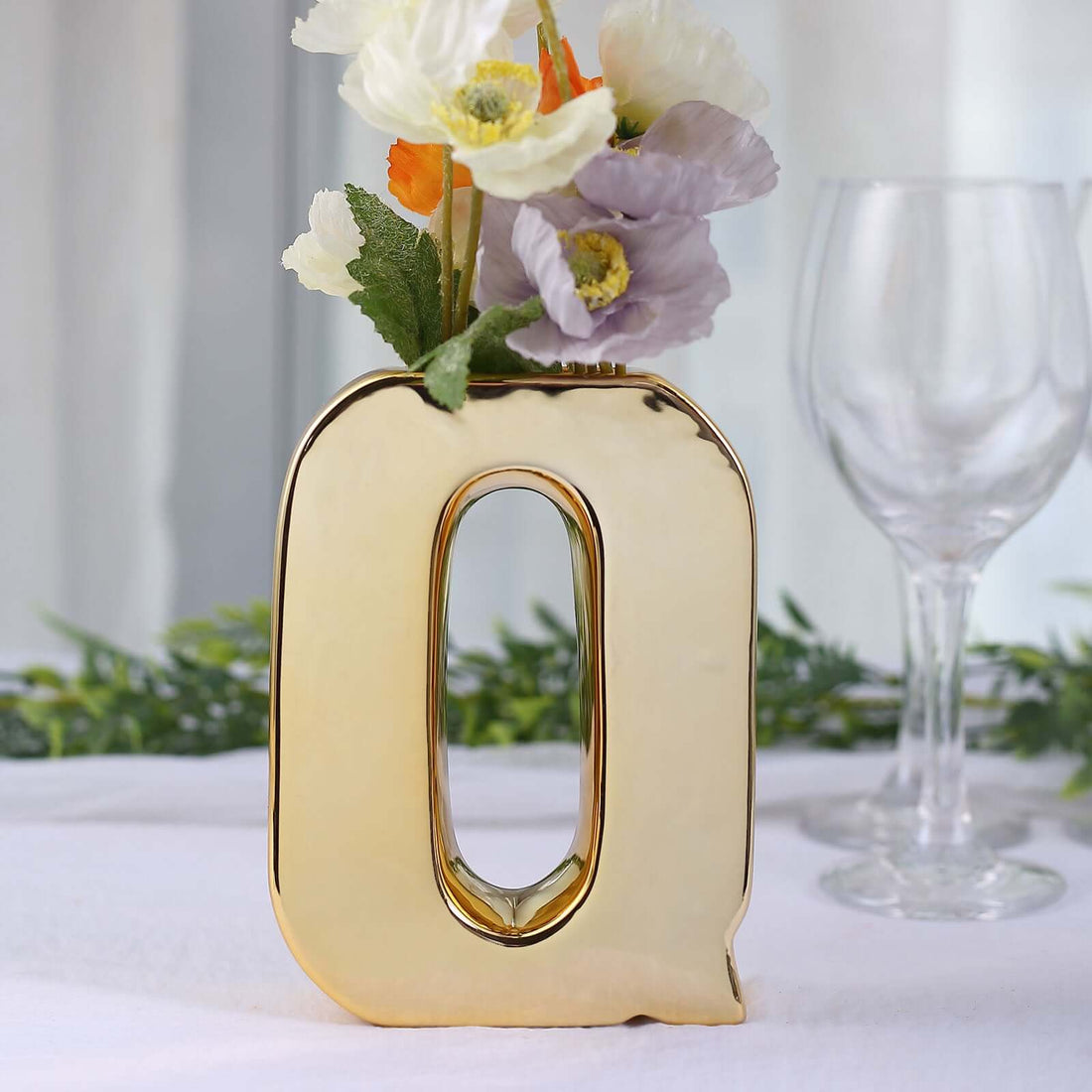 Gold letter Q vase with flowers beside a glass, elegant decor piece.
