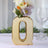 Gold letter Q vase with flowers beside a glass, elegant decor piece.