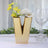 Gold V-shaped vase with yellow flowers and greenery.